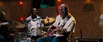 Movie still from “Black Snake Moan” (2006), directed by Craig Brewer – A man playing a guitar while another man plays drums; Medium shot, Low angle