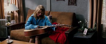 Movie still from “Black Snake Moan” (2006), directed by Craig Brewer – A woman sitting on a couch playing a guitar; Medium shot, High angle