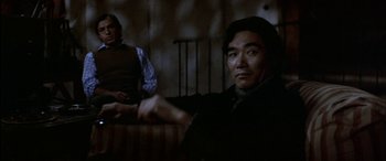 Movie still from “Black Sunday” (1977), directed by John Frankenheimer – A man sitting on a couch next to another man; Medium shot, Low angle