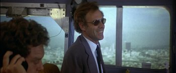 Movie still from “Black Sunday” (1977), directed by John Frankenheimer – A man in a suit and sunglasses smiling for the camera; Medium shot, Low angle