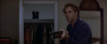 Movie still from “Black Sunday” (1977), directed by John Frankenheimer – A man holding a gun in a room with clothes on; Close Up shot, Over the shoulder angle