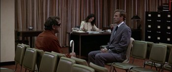 Movie still from “Black Sunday” (1977), directed by John Frankenheimer – Two men and a woman sitting at a table; Wide shot, Over the shoulder angle