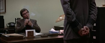 Movie still from “Black Sunday” (1977), directed by John Frankenheimer – A man in a business suit sitting at a desk; Medium shot, Over the shoulder angle
