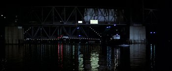 Movie still from “Black Sunday” (1977), directed by John Frankenheimer – A boat on a river at night with a bridge in the background; Extreme Wide shot, Low angle