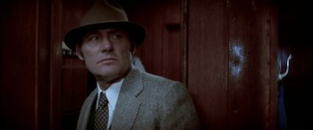 Movie still from “Black Sunday” (1977), directed by John Frankenheimer – A person wearing a suit and a hat; Close Up shot, Over the shoulder angle