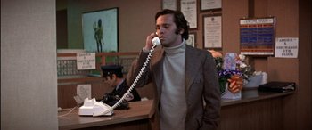 Movie still from “Black Sunday” (1977), directed by John Frankenheimer – A man talking on a phone while standing in front of a counter; Medium shot, High angle