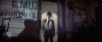 Movie still from “Black Sunday” (1977), directed by John Frankenheimer – A man wearing a hat and a suit standing in front of a building; Medium shot, Low angle