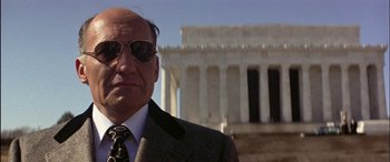 Movie still from “Black Sunday” (1977), directed by John Frankenheimer – An older man wearing a suit and sunglasses in front of the lincoln memorial in washington , d; Close Up shot, Low angle