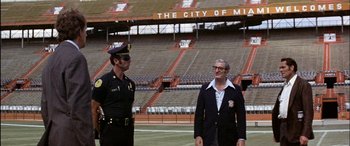 Movie still from “Black Sunday” (1977), directed by John Frankenheimer – Two police officers standing next to each other on a field; Extreme Wide shot, Low angle