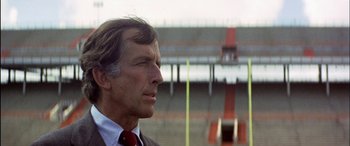 Movie still from “Black Sunday” (1977), directed by John Frankenheimer – A man in a suit and tie standing in front of an empty stadium; Close Up shot, Low angle