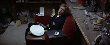 Movie still from “Black Sunday” (1977), directed by John Frankenheimer – A man sitting in a red chair holding a book; Medium shot, Overhead angle