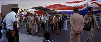 Movie still from “Black Sunday” (1977), directed by John Frankenheimer – A group of people standing in front of airplanes on a runway; Wide shot, High angle