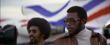 Movie still from “Black Sunday” (1977), directed by John Frankenheimer – Two black men wearing glasses and a brown jacket; Close Up shot, Low angle