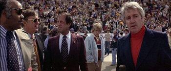 Movie still from “Black Sunday” (1977), directed by John Frankenheimer – A man in a red jacket and a tie in front of a crowd of onlookers; Medium shot, High angle