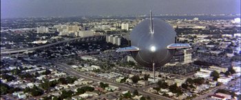 Movie still from “Black Sunday” (1977), directed by John Frankenheimer – An aerial view of a city with a large object in the middle of it; Extreme Wide shot, Low angle