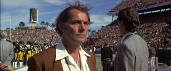 Movie still from “Black Sunday” (1977), directed by John Frankenheimer – A man in a brown jacket is standing in front of a crowd; Close Up shot, Low angle