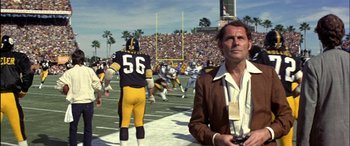 Movie still from “Black Sunday” (1977), directed by John Frankenheimer – A man in a brown jacket is on a football field; Medium shot, Low angle