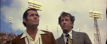 Movie still from “Black Sunday” (1977), directed by John Frankenheimer – A couple of men standing next to each other in a stadium; Close Up shot, Low angle