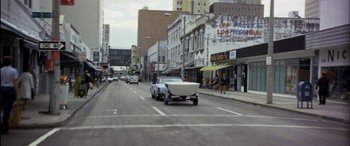 Movie still from “Black Sunday” (1977), directed by John Frankenheimer – A car driving down a street with a boat on the back of it; Extreme Wide shot, High angle
