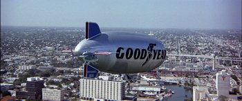 Movie still from “Black Sunday” (1977), directed by John Frankenheimer – A very large silver and blue blimp flying over a city; Extreme Wide shot, Low angle