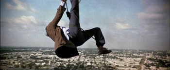 Movie still from “Black Sunday” (1977), directed by John Frankenheimer – A man hanging from the side of a building on a rope; Wide shot, Low angle