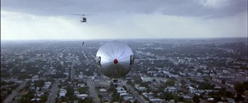 Movie still from “Black Sunday” (1977), directed by John Frankenheimer – A silver balloon flying over a city with a helicopter in the background; Extreme Wide shot, Low angle