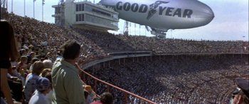 Movie still from “Black Sunday” (1977), directed by John Frankenheimer – A crowd of people in a stadium with an air ship in the background; Extreme Wide shot, Low angle