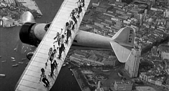 Movie still from “Blame It on Rio” (1984), directed by Stanley Donen – An aerial view of people standing on the wing of an airplane; Wide shot, Overhead angle