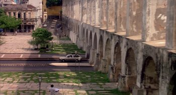 Movie still from “Blame It on Rio” (1984), directed by Stanley Donen – A car parked on the side of a road next to a stone wall; Extreme Wide shot, High angle