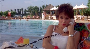 Movie still from “Blame It on Rio” (1984), directed by Stanley Donen – A woman sitting at the edge of a pool talking on the phone; Medium shot, Low angle