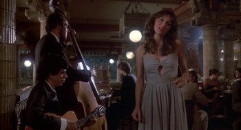 Movie still from “Blame It on Rio” (1984), directed by Stanley Donen – A woman in a dress standing in front of a guitar; Medium shot, Low angle