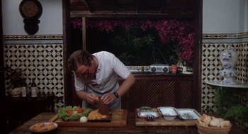 Movie still from “Blame It on Rio” (1984), directed by Stanley Donen – A man cutting a piece of meat on a cutting board; Medium shot, Low angle