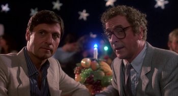 Movie still from “Blame It on Rio” (1984), directed by Stanley Donen – Two men sitting next to each other in front of a cake; Medium shot, Low angle