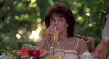 Movie still from “Blame It on Rio” (1984), directed by Stanley Donen – A woman sitting at a table drinking a glass of orange juice; Close Up shot, Over the shoulder angle