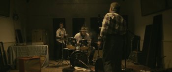 Movie still from “Blaze” (2018), directed by Ethan Hawke – A group of people that are sitting around a drum set; Wide shot, Over the shoulder angle
