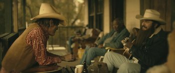 Movie still from “Blaze” (2018), directed by Ethan Hawke – A group of people sitting on a porch; Medium shot, Over the shoulder angle