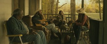 Movie still from “Blaze” (2018), directed by Ethan Hawke – A group of people sitting on a porch playing guitars; Wide shot, Over the shoulder angle