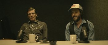 Movie still from “Blaze” (2018), directed by Ethan Hawke – Two men sitting at a table in front of coffee cups; Medium shot, Over the shoulder angle