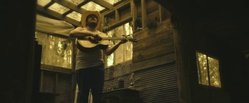 Movie still from “Blaze” (2018), directed by Ethan Hawke – A man in a straw hat playing a guitar; Medium shot, Low angle