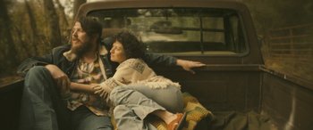 Movie still from “Blaze” (2018), directed by Ethan Hawke – A woman sitting on the back of a car next to a man; Medium shot, Overhead angle