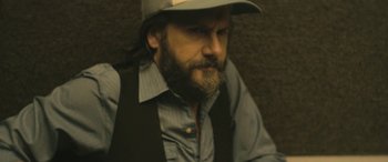 Movie still from “Blaze” (2018), directed by Ethan Hawke – A man with a beard wearing a hat and vest; Close Up shot, Over the shoulder angle