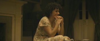 Movie still from “Blaze” (2018), directed by Ethan Hawke – A woman sitting on the ground with her hands clasped together; Medium shot, Over the shoulder angle