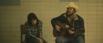 Movie still from “Blaze” (2018), directed by Ethan Hawke – A man and a woman sitting next to each other playing a guitar; Medium shot, High angle