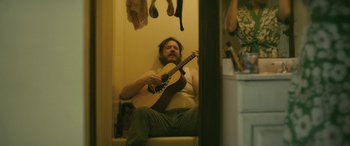 Movie still from “Blaze” (2018), directed by Ethan Hawke – A man sitting on a chair holding a guitar; Medium shot, Low angle
