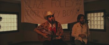 Movie still from “Blaze” (2018), directed by Ethan Hawke – A man in a cowboy hat singing into a guitar; Wide shot, High angle