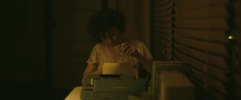 Movie still from “Blaze” (2018), directed by Ethan Hawke – A woman sitting in front of a typewriter looking at a piece of paper; Medium shot, High angle