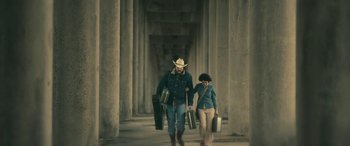 Movie still from “Blaze” (2018), directed by Ethan Hawke – A man and a woman walking down a walkway holding suitcases; Wide shot, Low angle