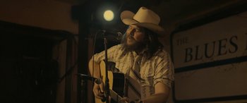 Movie still from “Blaze” (2018), directed by Ethan Hawke – A man in a cowboy hat playing a guitar; Medium shot, Low angle