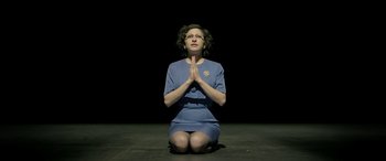 Movie still from “Blaze” (2018), directed by Ethan Hawke – A woman sitting on the ground with her hands in prayer position; Medium shot, High angle