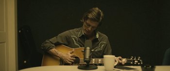 Movie still from “Blaze” (2018), directed by Ethan Hawke – A man sitting at a table playing a guitar; Medium shot, High angle